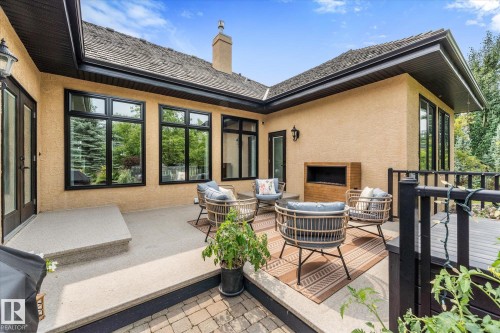 Expansive patio featuring a built-in outdoor fireplace, stucco exterior, black-framed windows, and a multi-level design with a paver stone area - #52 Riverstone Close, Rural Sturgeon County, AB - Outdoor With Deck Patio Veranda With Exterior