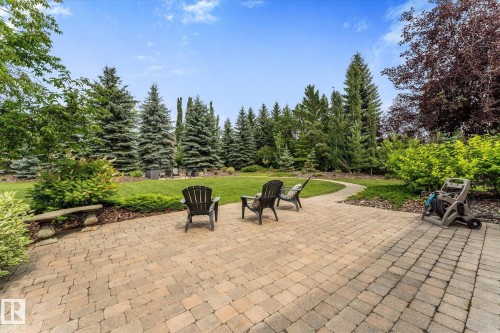Expansive paver patio with a curved stone pathway, surrounded by mature evergreen trees, lush green lawn, and diverse landscaping - #52 Riverstone Close, Rural Sturgeon County, AB - Outdoor