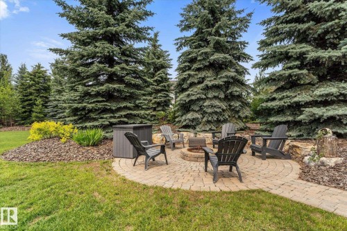 Outdoor entertaining area featuring a paver patio with a built-in fire pit, surrounded by mature evergreen trees - #52 Riverstone Close, Rural Sturgeon County, AB - Outdoor