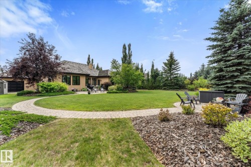Spacious backyard featuring a large green lawn, mature trees, and a paved stone pathway leading to a patio area - #52 Riverstone Close, Rural Sturgeon County, AB - Outdoor
