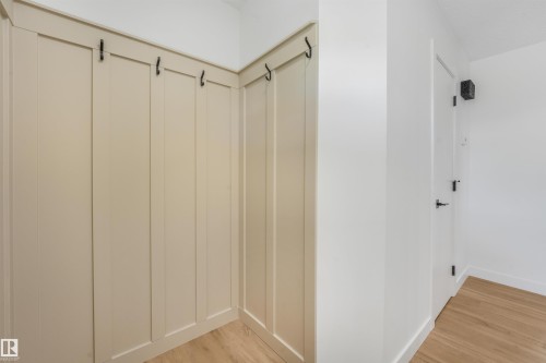 Built-in board and batten wall paneling with black coat hooks, light wood-finish flooring, and a white interior door with black hardware - #39 14511 52 Street Nw, Edmonton, AB - Indoor Photo Showing Other Room