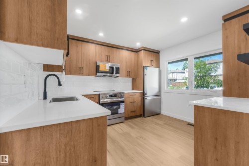 Kitchen featuring wood-finish cabinetry, stainless steel appliances, white subway tile backsplash, and light wood-finish flooring - #39 14511 52 Street Nw, Edmonton, AB - Indoor Photo Showing Kitchen With Upgraded Kitchen
