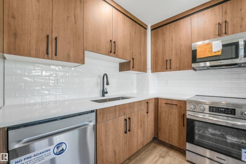 Contemporary kitchen featuring light wood-finish cabinetry, white subway tile backsplash, white countertops, stainless steel appliances, and a matte black faucet - #39 14511 52 Street Nw, Edmonton, AB - Indoor Photo Showing Kitchen With Upgraded Kitchen