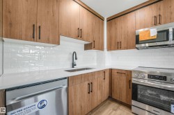 Contemporary kitchen featuring light wood-finish cabinetry, white subway tile backsplash, white countertops, stainless steel appliances, and a matte black faucet - 
