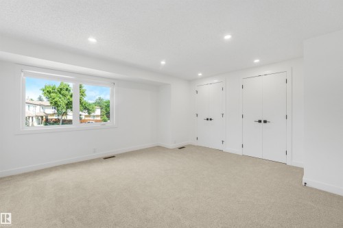 Spacious room featuring neutral carpeting, a large window, white walls, recessed lighting, and two sets of double doors with black hardware - #39 14511 52 Street Nw, Edmonton, AB - Indoor Photo Showing Other Room