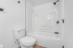 Bathroom featuring a white bathtub and shower combination with dark-finished fixtures, a white toilet, and wood-finish flooring - 