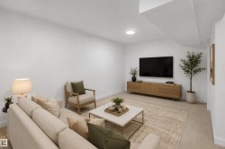 Recessed ceiling lighting, wall-mounted television, wood-finish media console, light-toned carpeting, and a square coffee table with a light-colored surface - 