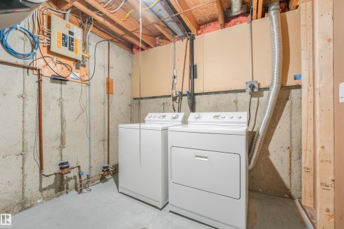 Dedicated laundry area featuring a white washing machine and dryer, exposed concrete walls, and visible utility infrastructure including copper piping and electrical panel - #39 14511 52 Street Nw, Edmonton, AB - Indoor Photo Showing Laundry Room
