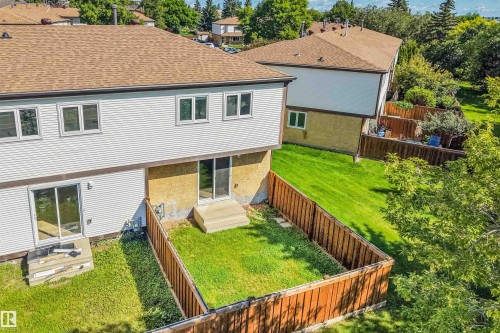 Rear exterior featuring white horizontal siding, a brown shingle roof, multiple windows, and two sliding glass doors leading to the fenced yard - #39 14511 52 Street Nw, Edmonton, AB - Outdoor With Exterior