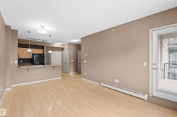 Open-concept living space featuring wood-finish flooring, a kitchen with light wood cabinetry and black appliances, a breakfast bar, and a balcony access door - 