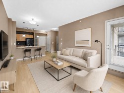 Open-concept living area featuring light wood-finish flooring, a kitchen with dark appliances and wood cabinetry, a breakfast bar, and a balcony access door - 