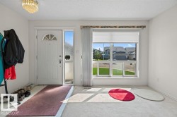 Entryway featuring a white paneled door with an arched decorative window, an adjacent sidelight, and a multi-pane window with a pleated shade - 