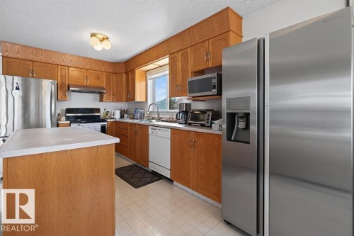 Kitchen featuring light wood cabinetry, a central island with a solid surface countertop, stainless steel appliances, and a window above the sink - 1046 Jones Crescent Nw, Edmonton, AB - Indoor Photo Showing Kitchen With Double Sink