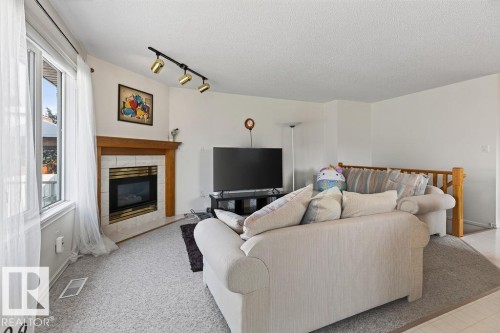 Living area featuring a gas fireplace with a tiled surround and wood mantel, large windows with white trim, track lighting, and light-colored carpeting - 1046 Jones Crescent Nw, Edmonton, AB - Indoor Photo Showing Living Room With Fireplace