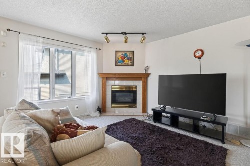 Living space featuring a corner fireplace with a wood mantel and tile surround, track lighting, and a large window with blinds - 1046 Jones Crescent Nw, Edmonton, AB - Indoor Photo Showing Living Room With Fireplace