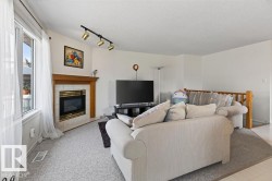 Living area featuring a gas fireplace with a tiled surround and wood mantel, large windows with white trim, track lighting, and light-colored carpeting - 