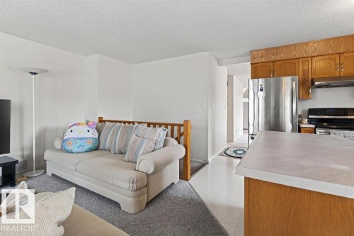Open-concept kitchen and living area featuring wood cabinetry, stainless steel refrigerator, dark cooking range, light-toned countertops, and light-colored flooring - 1046 Jones Crescent Nw, Edmonton, AB - Indoor