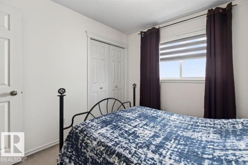 Bright bedroom featuring a large window with privacy blinds and dark drapes, a white paneled door, and a built-in closet with bi-fold doors - 1046 Jones Crescent Nw, Edmonton, AB - Indoor Photo Showing Bedroom