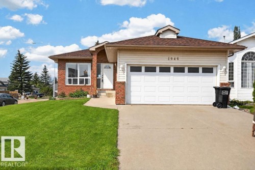 Brick and siding exterior featuring a white garage door with upper window inserts, a concrete driveway, and a manicured front lawn - 1046 Jones Crescent Nw, Edmonton, AB - Outdoor