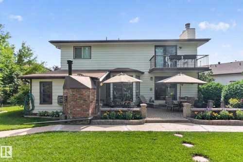 Expansive backyard featuring a manicured lawn, a two-tier paver patio, a built-in brick outdoor fireplace, and raised garden beds with stone caps - 18132 78 Avenue Nw, Edmonton, AB - Outdoor With Balcony With Deck Patio Veranda