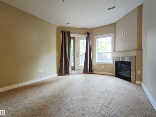 Inviting living area featuring a corner fireplace with a tiled surround and mantel, a glass-paned door, and a multi-pane window - #21 11518 76 Av Nw, Edmonton, AB - Indoor With Fireplace