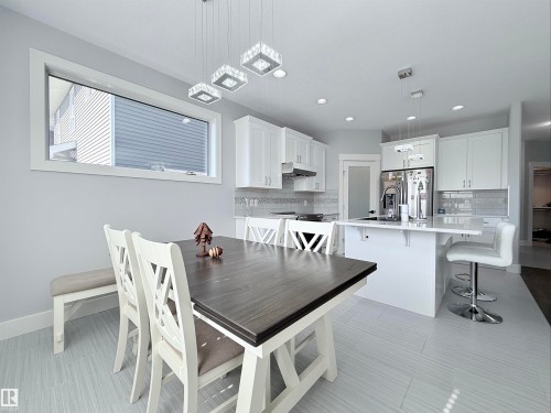 Modern kitchen and dining area featuring white cabinetry, a kitchen island with seating, stainless steel appliances, and sleek tile flooring - 8719 218 Street Nw, Edmonton, AB - Indoor
