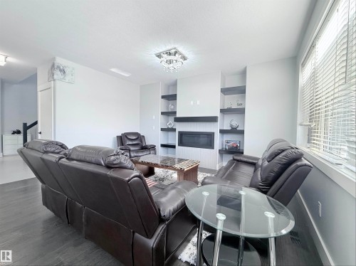 Living area featuring dark wood-finish flooring, a wall-mounted electric fireplace, built-in shelving, and a large window with blinds - 8719 218 Street Nw, Edmonton, AB - Indoor Photo Showing Living Room With Fireplace