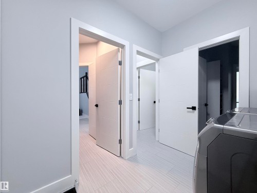 Hallway featuring light gray walls, white trim, and light wood-finish flooring - 8719 218 Street Nw, Edmonton, AB - Indoor Photo Showing Laundry Room