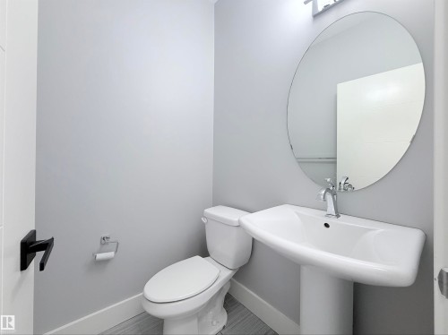 Pedestal sink with chrome faucet, oval mirror, and light gray walls - 8719 218 Street Nw, Edmonton, AB - Indoor Photo Showing Bathroom