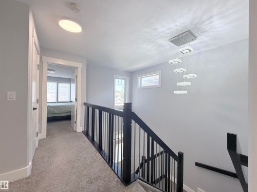 Upper-level hallway featuring a modern multi-tiered chandelier and gray carpet flooring - 8719 218 Street Nw, Edmonton, AB - Indoor Photo Showing Other Room