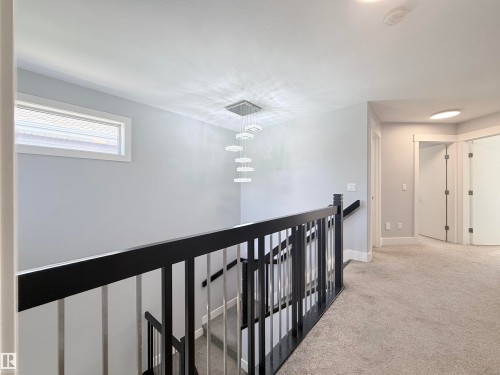 Upper landing with plush carpeting, modern chandelier, sleek black and metal railings, white trim, and a horizontal window - 8719 218 Street Nw, Edmonton, AB - Indoor Photo Showing Other Room
