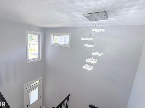 Foyer entry with a contemporary tiered chandelier, multiple windows, and a frosted glass panel door - 8719 218 Street Nw, Edmonton, AB - Indoor Photo Showing Other Room