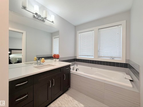 Bright bathroom featuring a dark wood-finish vanity with a white countertop and undermount sink, a large mirror, and a built-in tub with tile surround - 8719 218 Street Nw, Edmonton, AB - Indoor Photo Showing Bathroom