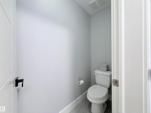 Compact lavatory featuring a white toilet, light gray walls, and wood-finish flooring - 8719 218 Street Nw, Edmonton, AB - Indoor Photo Showing Bathroom