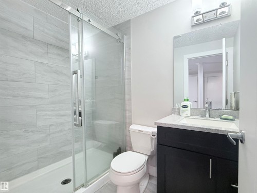 Bathroom featuring a glass-enclosed shower with tile surround, a dark wood-finish vanity with a light-toned countertop, and a contemporary vanity light fixture - 8719 218 Street Nw, Edmonton, AB - Indoor Photo Showing Bathroom