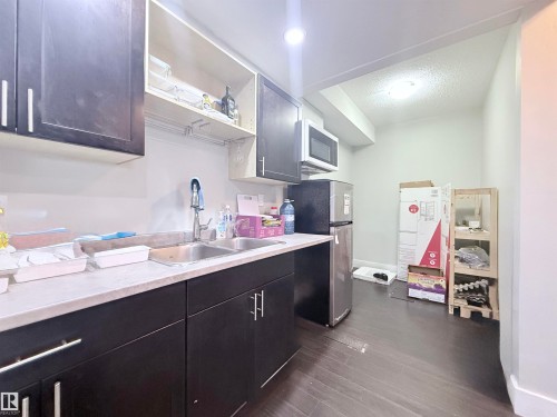 Compact kitchen space featuring dark cabinetry, a double basin sink, and wood-finish flooring - 8719 218 Street Nw, Edmonton, AB - Indoor Photo Showing Kitchen With Double Sink
