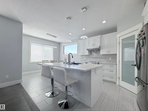 Spacious kitchen featuring an island with seating, white shaker-style cabinetry, stainless steel appliances, and tile flooring - 8719 218 Street Nw, Edmonton, AB - Indoor Photo Showing Kitchen With Upgraded Kitchen