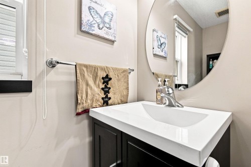 Modern bathroom featuring a sleek rectangular vessel sink set atop a dark cabinetry vanity with white quartz countertop, chrome faucet fixture, and round mirror with integrated lighting - 204 59 Street Sw, Edmonton, AB - Indoor Photo Showing Bathroom