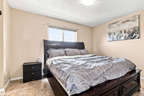 Spacious bedroom featuring a black leather upholstered bed frame, tile flooring, neutral wall finishes, a window with natural light, and a coordinating nightstand with drawer storage - 204 59 Street Sw, Edmonton, AB - Indoor Photo Showing Bedroom