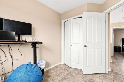 Versatile bedroom featuring tile flooring, a wall-mounted desk with shelving, and a spacious double-door closet with six-panel white doors - 204 59 Street Sw, Edmonton, AB - Indoor Photo Showing Other Room