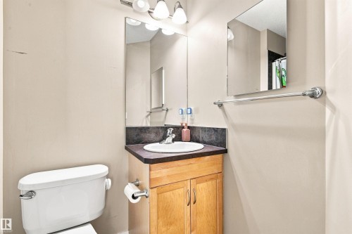 Corner vanity with a white basin sink, dark countertop, and wood-finish cabinetry - 204 59 Street Sw, Edmonton, AB - Indoor Photo Showing Bathroom