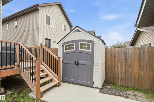 Raised wood deck with black metal balusters, wood stairs, and a detached storage shed with gray doors - 204 59 Street Sw, Edmonton, AB - Outdoor With Exterior