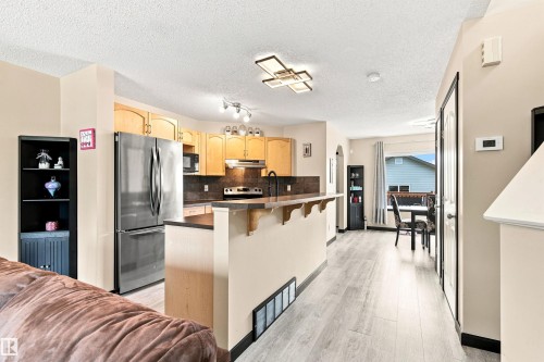 Kitchen featuring wood cabinetry, stainless steel refrigerator, and dark countertops - 204 59 Street Sw, Edmonton, AB - Indoor Photo Showing Kitchen