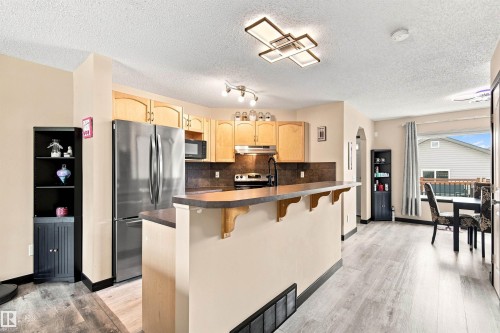 Kitchen featuring light wood-finish cabinetry, stainless steel appliances, and a breakfast bar - 204 59 Street Sw, Edmonton, AB - Indoor Photo Showing Kitchen