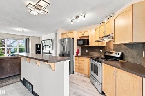 Kitchen featuring wood-finish cabinetry, stainless steel appliances, dark countertops, and tile backsplash - 204 59 Street Sw, Edmonton, AB - Indoor Photo Showing Kitchen With Upgraded Kitchen