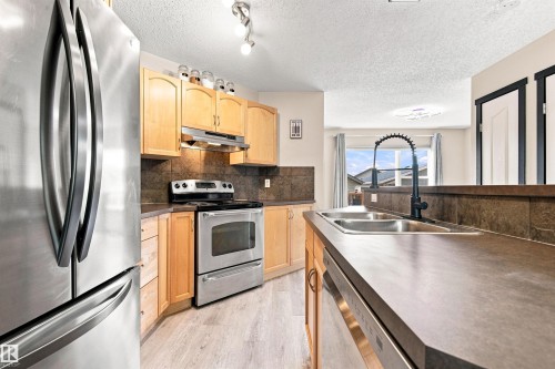 Kitchen featuring stainless steel appliances, wood-finish cabinetry, a double basin sink with a matte black faucet, and durable countertops - 204 59 Street Sw, Edmonton, AB - Indoor Photo Showing Kitchen With Double Sink
