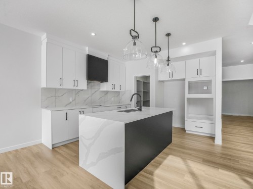 Spacious kitchen featuring an oversized island with a waterfall countertop, white cabinetry with matte black hardware, and wood-finish flooring - 239 Kinglet Boulevard Nw, Edmonton, AB - Indoor Photo Showing Kitchen With Upgraded Kitchen