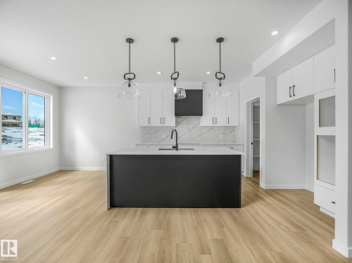 Modern kitchen featuring a dark island with an integrated sink, light wood-finish flooring, white upper and lower cabinetry, and a patterned backsplash - 239 Kinglet Boulevard Nw, Edmonton, AB - Indoor Photo Showing Kitchen With Upgraded Kitchen