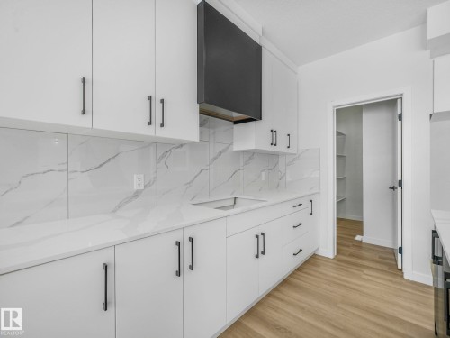 Modern kitchen featuring white cabinetry, a black range hood, and light-colored countertops with a matching backsplash - 239 Kinglet Boulevard Nw, Edmonton, AB - Indoor