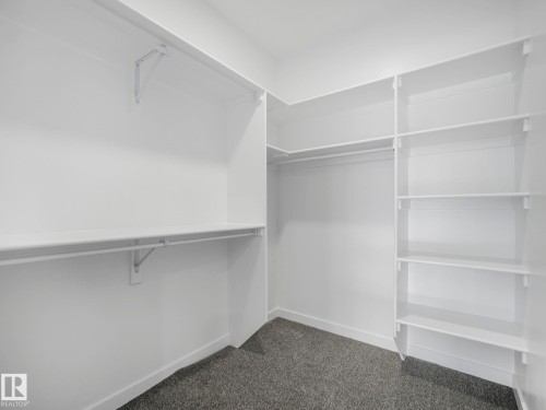 Walk-in closet featuring white wall shelving, hanging rods, and dark gray carpet flooring - 239 Kinglet Boulevard Nw, Edmonton, AB - Indoor With Storage